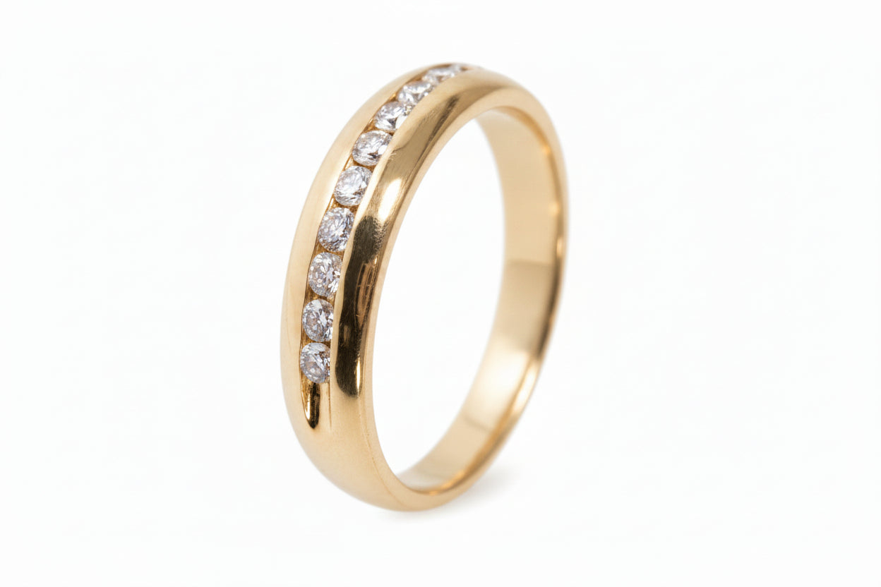 A yellow gold wedding band featuring round diamonds set on the upper half of the band.
